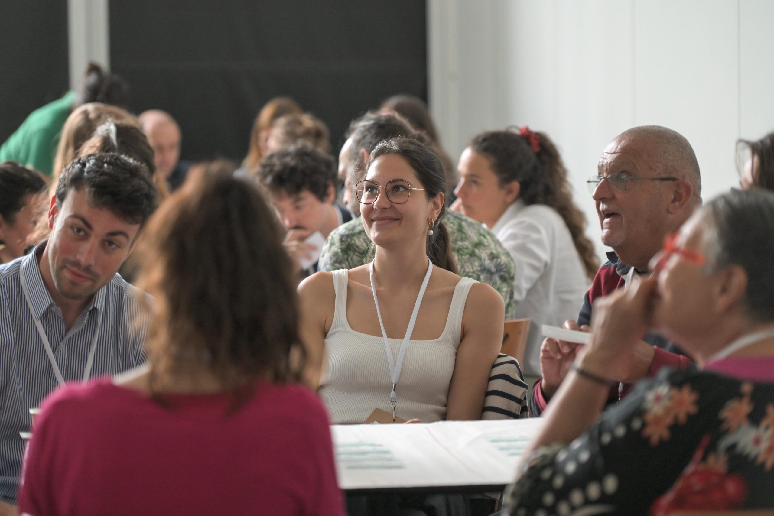 Des participants assis autour de tables de travail, en échange lors d’un forum animé par bluenove
