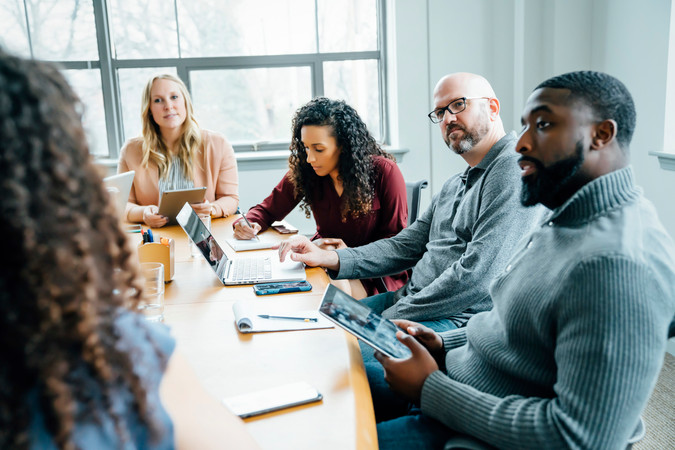 Réunion de dialogue social autour d’une table, collaborateurs échangeant avec ordinateurs et tablettes